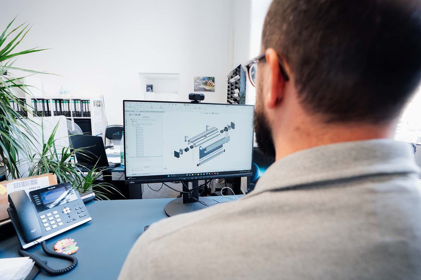 Employee at a desk in front of a screen showing a technical 3D design